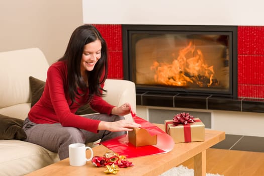 Happy woman in red wrapping Christmas present by home fireplace