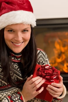 Xmas present happy woman by home fireplace wear Santa hat