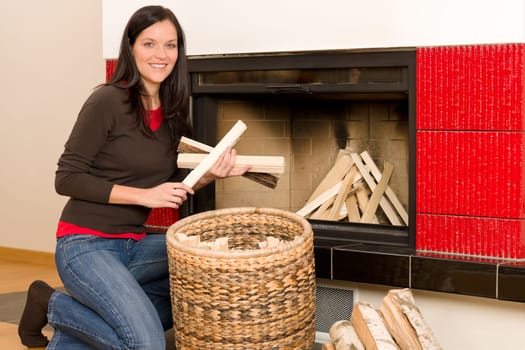 Young woman putting wood logs from wickerwork basket into fireplace