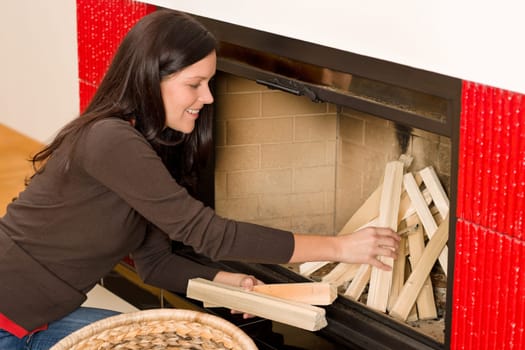 Young woman putting wood logs from wickerwork basket into fireplace