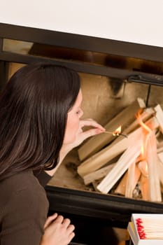 Young woman lighting up wood logs in fireplace home living