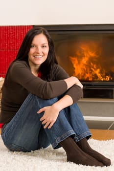 Beautiful happy young woman sitting front of home fireplace