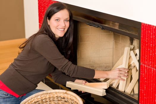 Young woman putting wood logs from wickerwork basket into fireplace
