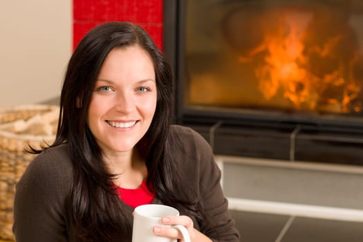 Young woman enjoying winter hot drink by home fireplace