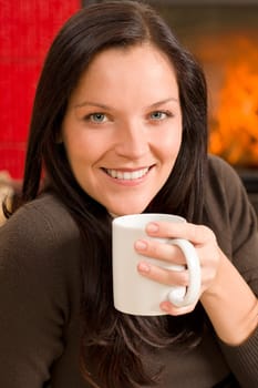 Young woman enjoying winter hot drink by home fireplace