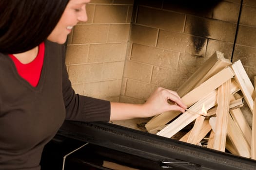 Young woman lighting up wood logs in fireplace home living