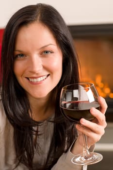 Young woman enjoying glass of red wine by home fireplace
