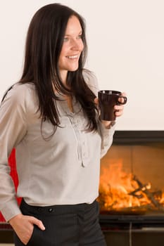 Young woman enjoying winter hot drink by home fireplace