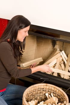 Young woman putting wood logs from wickerwork basket into fireplace