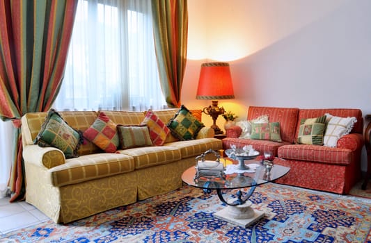 Elegant living room with classic looking sofa, colorful curtains, lamp and glass table