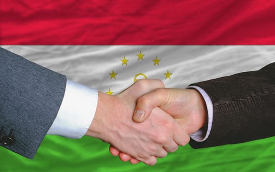 two businessmen shaking hands after good business investment  agreement in tajikistan, in front of flag