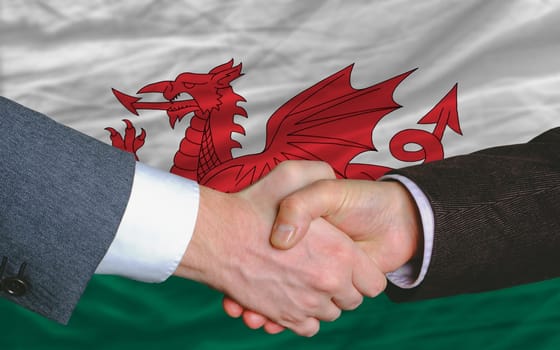 two businessmen shaking hands after good business investment  agreement in wales, in front of flag