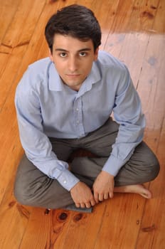 smiling attractive young man sitting on wooden floor at home
