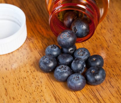 Fresh blueberries being poured from orange prescription bottle onto wooden table for breakfast