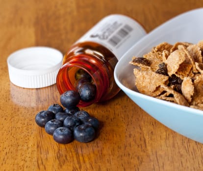 Fresh blueberries being poured from orange prescription bottle onto wooden table for breakfast with fiber cereal in a bowl