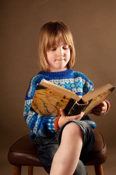 Child reading book. studio image of blond boy against brown background studying a text book