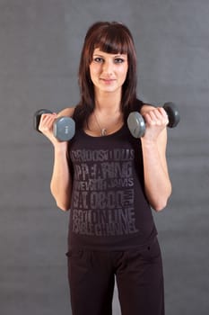 young woman lifting weights on gray background