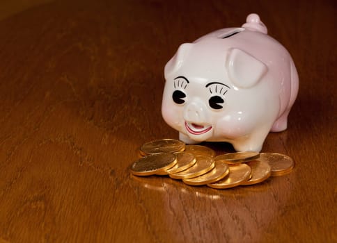 Pink piggybank on a wooden table with pile of gold eagle coins