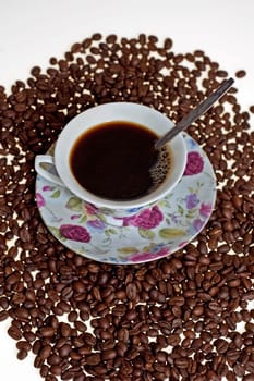 A cup in a pile of coffe beans on white background.