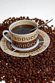 A cup in a pile of coffe beans on white background.