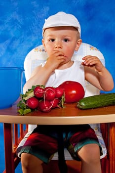 Short boy playing with vegetables against the blue mosaic background