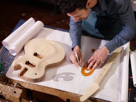 mid adult man at work as craftsman in italian workshop with guitars and blueprints, drawing sketches. High angle view