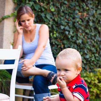 Young woman on the phone and a little boy outdoors.