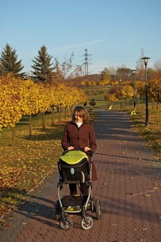 Young mother is walking in park with baby carriage