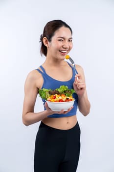 Young sporty Asian woman in sportswear holding salad bowl fill with vibrant of fruit and vegetable. Natural youthful and fit body lifestyle with balance nutrition on isolated background. Vigorous