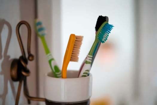 Toothbrushes in a glass attached to a mirror, personal hygiene products to take care of the cleanliness and health of the oral cavity, gums and teeth at home in the bathroom.