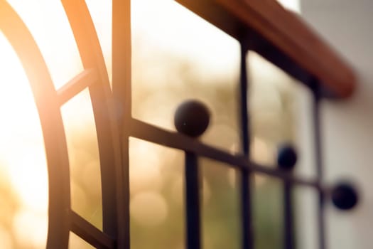 Forged stylish gates with an elegance decor, a fence on the veranda with curved lines against the backdrop of a sunny evening, close-up view.