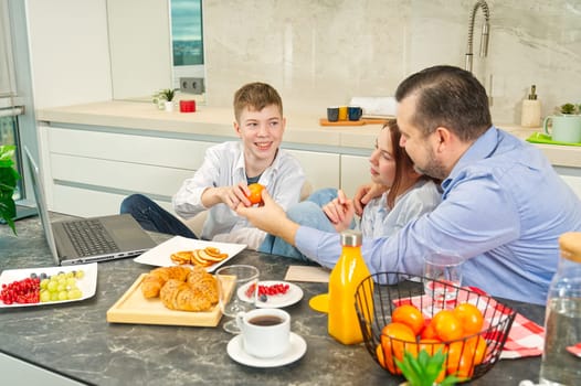 Young family with school kids have fun at breakfast time. Happy family eating healthy breakfast. Quality time with Family in kitchen eating together. Family Using Digital Devices At Breakfast