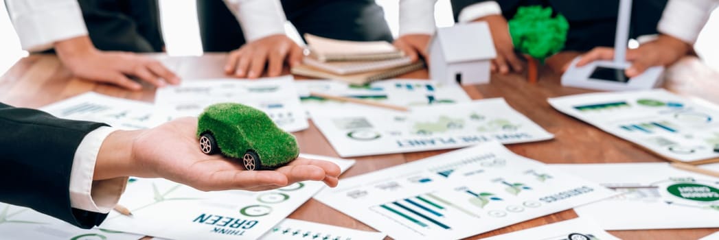 Businessman holding green EV car model mock in electric car company meeting, business people planning strategic marketing for eco-friendly vehicle product using clean energy with net zero.Trailblazing