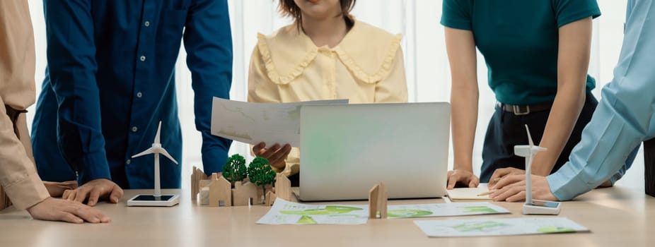 Professional business team prepare to present green business on table with windmill presented using renewable energy, wooden block and environmental document scatter around. Closeup. Delineation.