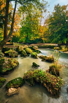 Munich English garden Englischer garten park and Eisbach river with artificial waterfall . Autumn colours on trees and leaves and flowing river. Munchen, Bavaria, Germany