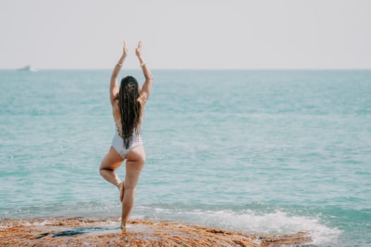 Woman sea yoga. Back view of free calm happy satisfied woman with long hair standing on top rock with yoga position against of sky by the sea. Healthy lifestyle outdoors in nature, fitness concept.