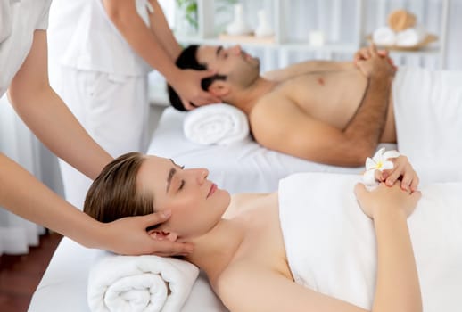Caucasian couple enjoying relaxing anti-stress head massage and pampering facial beauty skin recreation leisure in dayspa modern light ambient at luxury resort or hotel spa salon. Quiescent