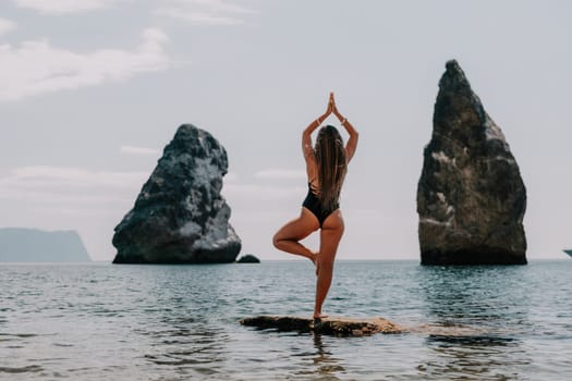 Woman meditating in yoga pose silhouette at the ocean, beach and rock mountains. Motivation and inspirational fit and exercising. Healthy lifestyle outdoors in nature, fitness concept.