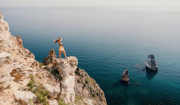 Woman travel sea. Happy tourist taking picture outdoors for memories. Woman traveler looks at the edge of the cliff on the sea bay of mountains, sharing travel adventure journey.