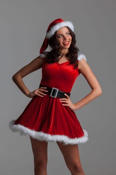 Portrait of a pretty young brunette woman in red dress and hat posing isolated over gray background
