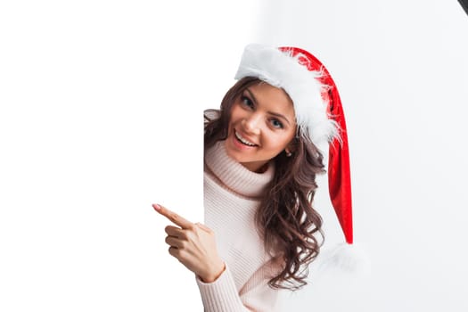 Portrait of happy girl with Christmas hat holding poster and pointing to copy space