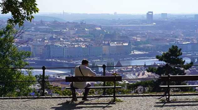 The capital of the Czech Republic is Prague. A bench in a beautiful place from where you can see the city. A man admires the panorama of a big city