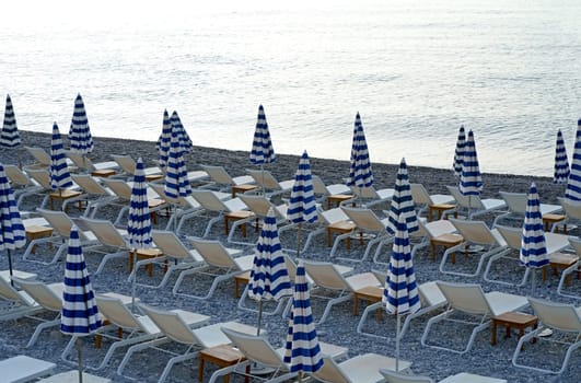 Striped blue and white umbrellas and sun loungers on the city beach. Umbrellas on the beach against the background of the sea