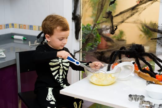 boy dressed as a skeleton preparing halloween cookies.Happy boy preparing for halloween. Festival in the kitchen..