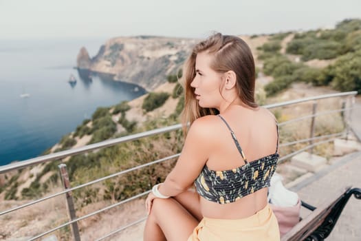 Woman travel sea. Happy tourist taking picture outdoors for memories. Woman traveler looks at the edge of the cliff on the sea bay of mountains, sharing travel adventure journey.