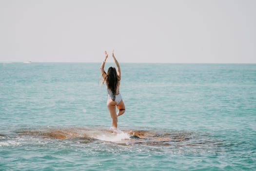 Woman sea yoga. Back view of free calm happy satisfied woman with long hair standing on top rock with yoga position against of sky by the sea. Healthy lifestyle outdoors in nature, fitness concept.