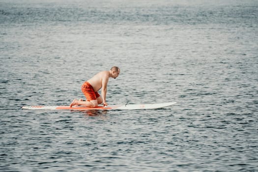 Active mature male paddler with his paddleboard and paddle on a sea at summer. Happy senior man stands with a SUP board. Stand up paddle boarding - outdor active recreation in nature