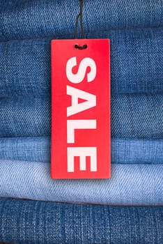 Red Sale Sign With Stack of Blue Jeans in Background