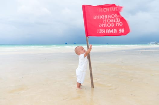 baby trying to grab a red flag on a tropical beach