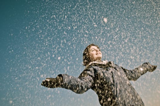 Young woman throwing snow on blue sky in background - joy and happines emotions